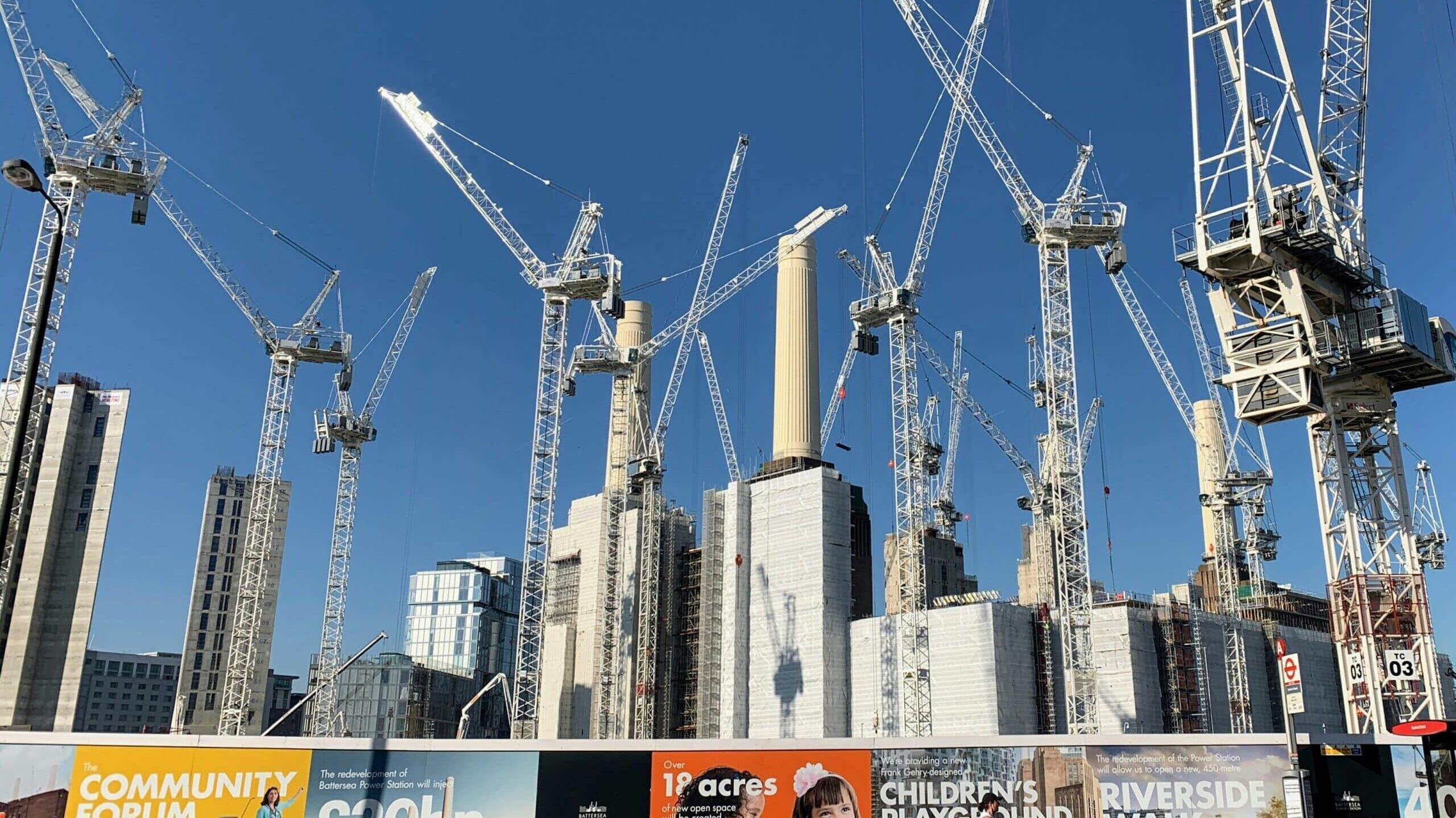 Ten white cranes towering over scaffolding on a construction site.