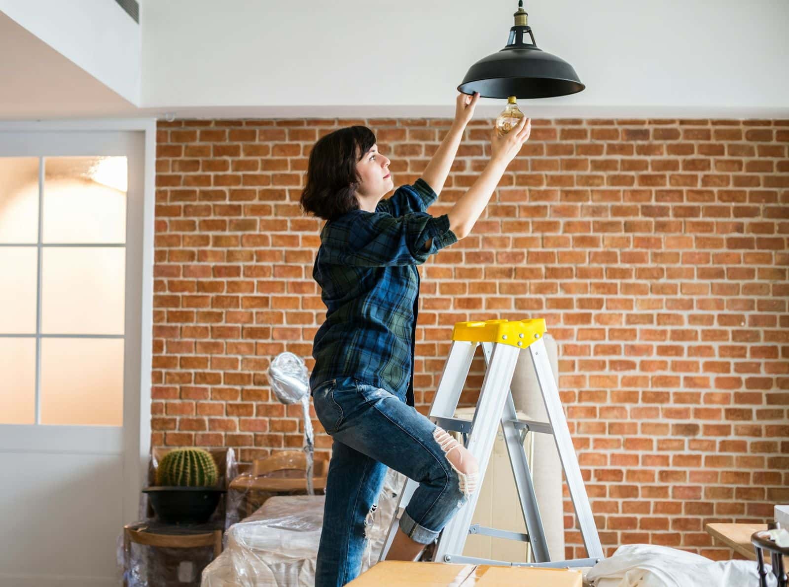 A woman on a stepladder fitting a light bulb in a rental property.